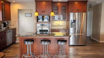 A kitchen with wooden cabinets, stainless steel appliances, a central island with stools, and pendant lighting.