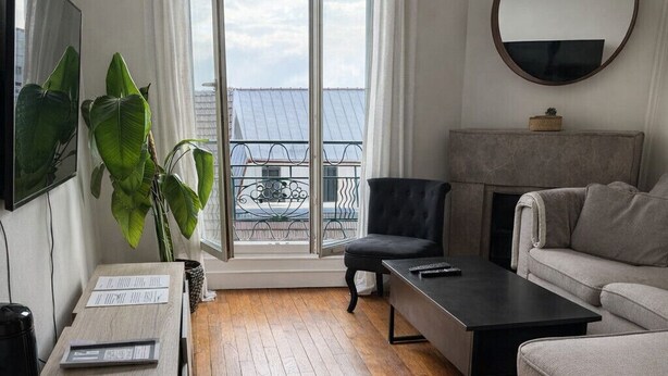 Ein modernes Wohnzimmer mit einer Couch, einem Couchtisch, einem Fernseher und einem großen Fenster mit Vorhängen.