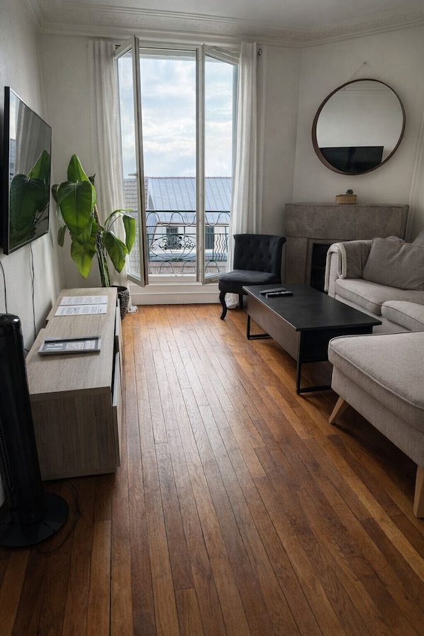 Un salon moderne avec un canapé, une table basse, un téléviseur et une grande fenêtre avec des rideaux.