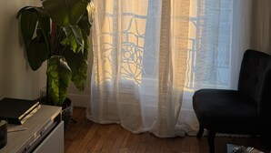 Ein Zimmer mit großem Fenster, einem Blumentopf, einem schwarzen Stuhl und Holzboden.