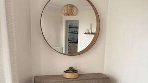 Ein Zimmer mit Kamin, einem runden Spiegel, einem blauen Sessel und einem grauen Sofa.