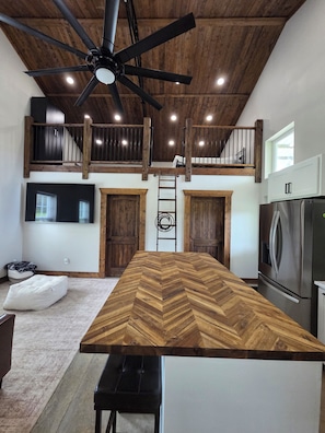 Una cocina moderna con encimera de madera en espiga, un ventilador de techo y un refrigerador de acero inoxidable.