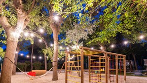 A playground with a wooden climbing structure, a hammock, and trees.