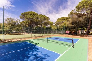 Ein Tennisplatz mit Netz, umgeben von Bäumen und einem Zaun.