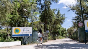 A cyclist on a paved path with a sign for 'Club del Sole Italia' and a fence on the right.