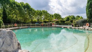 A clear swimming pool with a surrounding fence, lifebuoys, and a person in the background.