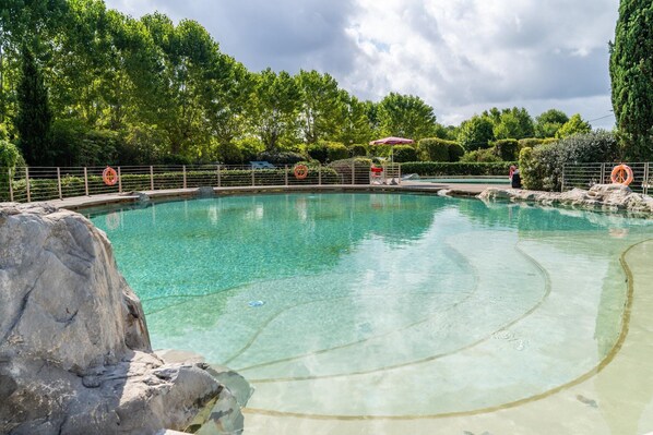 A clear swimming pool with a lifebuoy, surrounded by a fence, and a person standing in the background.