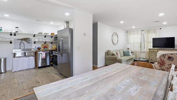 Una cocina moderna con electrodomésticos de acero inoxidable, un comedor con una mesa grande, un sofá y un televisor en la sala.