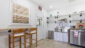 Una cocina con puerta blanca, ventana con persianas, refrigerador de acero inoxidable y un lavamanos.