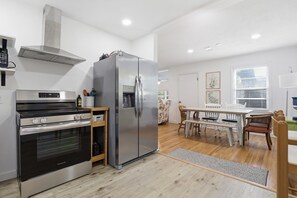 Une cuisine moderne équipée d’un réfrigérateur, d’un four et d’une hotte en acier inoxydable. On y trouve également un coin repas avec une table et des chaises en bois.