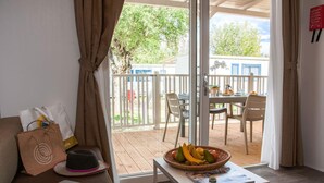 Ein Zimmer mit einer Couch, einem Laptop, einem Tisch mit Obstschale und Blick auf eine Terrassenanlage mit Stühlen und Tisch.