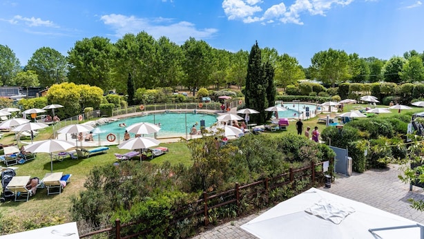 Ein Poolbereich mit mehreren Schwimmbecken, Liegestühlen, Sonnenschirmen und einem eingezäunten Garten.