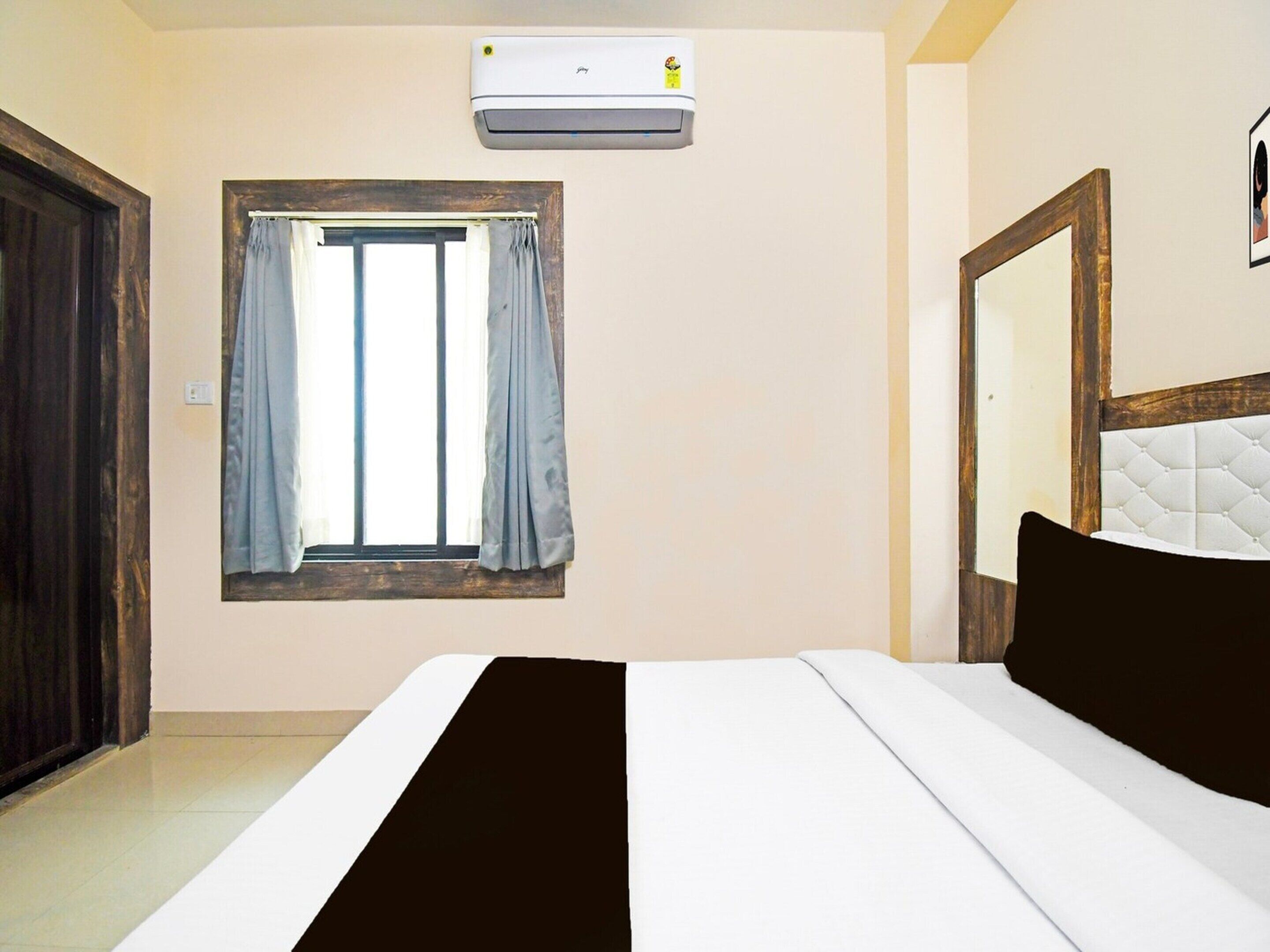 Une chambre à coucher avec un lit, une fenêtre avec des rideaux, un appareil de climatisation et une porte en bois.