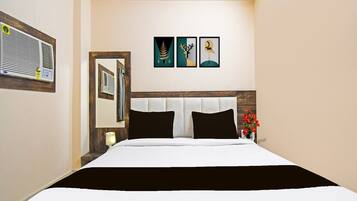 Habitación de hotel con cama, espejo, aire acondicionado de pared y tres obras de arte enmarcadas.