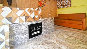 A reception area with a geometric-patterned counter, a sign reading 'Collection Company-Serviced,' a wooden wall, and a brown leather couch.