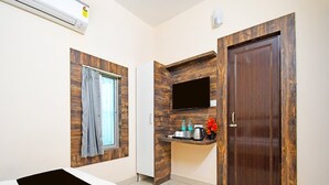 A hotel room with a bed, a TV mounted on a wooden wall, a small counter with toiletries, and a door.