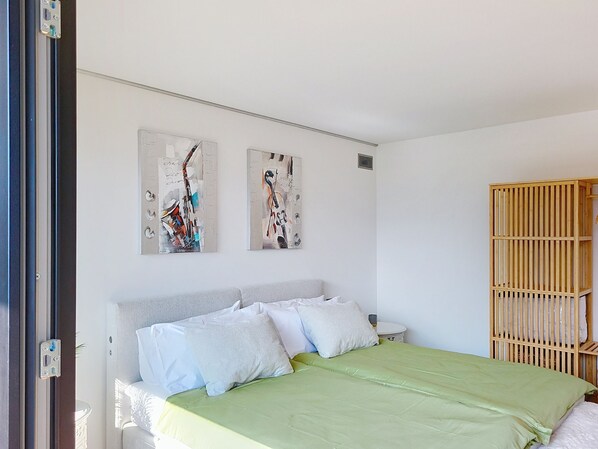 A bedroom with a bed, two wall-mounted paintings, a wooden wardrobe, and a white door.