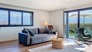 Ein modernes Wohnzimmer mit einer Couch, einem runden Couchtisch und Blick durch große Fenster.
