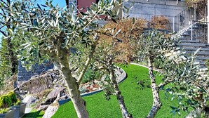 Ein angelegter Garten mit Olivenbäumen, einer Steinmauer und einer runden Rasenfläche.