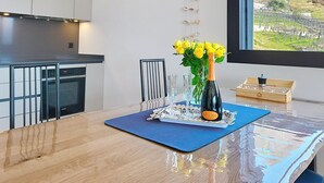 Eine moderne Küche mit Esstisch, einer gelb blühenden Vase, einer Champagnerflasche und Blick auf einen Weinberg durch ein Fenster.
