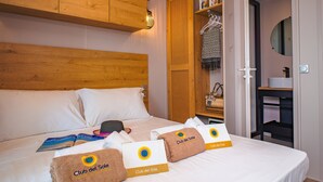 A hotel room with a wooden headboard, a bed with white linens, a wooden wardrobe, a bathroom with a round mirror, and towels with 'Club del Sole' branding. - Milano Marittima Boutique Resort (Cervia)