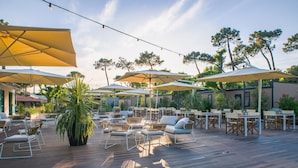 An outdoor patio with wooden flooring, multiple tables and chairs, and large umbrellas providing shade. - Milano Marittima Boutique Resort (Cervia)