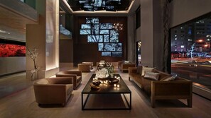 A modern lounge with sofas, a coffee table, and a large window with city lights visible outside.