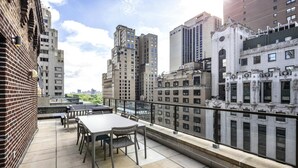 Terraço no telhado com mesa e cadeiras, com vista para um horizonte urbano repleto de edifícios.