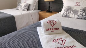 Ett hotellrum med två sängar, ett nattduksbord med en lampa och en dekorativ kudde med ett palmträdsmotiv.