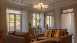 Una sala de estar con un sofá de cuero marrón, una lámpara colgante y ventanas amplias.