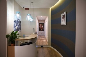 A hotel reception area with a curved counter, pendant lighting, a security camera, and a wall-mounted sign indicating a 50 suite with bed and breakfast. - 50 Suite B&B (Naples)