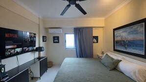 A bedroom with a bed, a TV mounted on the wall, a ceiling fan, and a painting. - Ocean View | Central SD | Rooftop Plunge Pool (Santo Domingo)