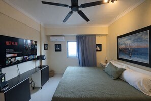 Ein Schlafzimmer mit einem Bett, einem an der Wand befestigten Fernseher, einem Deckenventilator und einem Gemälde.