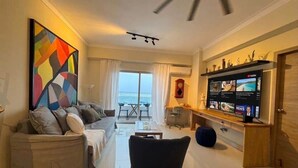 A living room with a sofa, a black chair, a TV, and a large painting. - Ocean View | Central SD | Rooftop Plunge Pool (Santo Domingo)