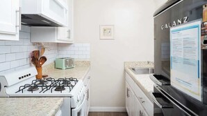 Eine kleine Küche mit weißen Schränken, einem Gasherd, einem Toaster und einem schwarzen Kühlschrank.
