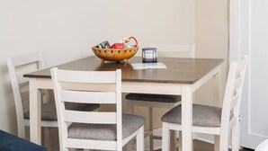 Ein Essbereich mit einem Holztisch, weißen Stühlen, einer Schale mit Gegenständen und einem Mülleimer.
