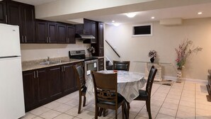 A kitchen with dark cabinets, a white refrigerator, a microwave, and a stove. There is a dining table with chairs and a vase with flowers. - Cozy 2BR Basement | Private Entry + Parking (Brampton)