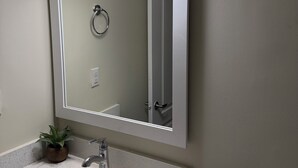 A bathroom with a large mirror, a sink, a towel rack, and a potted plant. - Cozy 2BR Basement | Private Entry + Parking (Brampton)