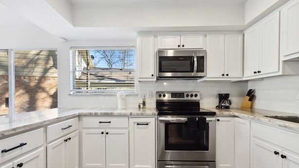 A modern kitchen with white cabinets, stainless steel appliances, and a large window. - Bright 3BR/2BA Home  Furnished w/yard + All Utilities Included near Lake Houston (Humble)
