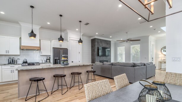 A modern kitchen with white cabinets, a central island with stools, a built-in oven, and a large TV. - Luxury Home on 30A~ 5 min walk to beach~ 4 bikes! (santa rosa beach)
