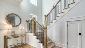 A staircase with wooden steps and black railings, a round mirror with a gold frame, a console table with lamps, and a door with a white panel. - Luxury Home on 30A~ 5 min walk to beach~ 4 bikes! (santa rosa beach)