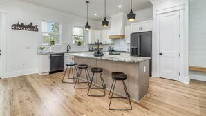 A modern kitchen with white cabinets, a central island with stools, pendant lighting, and a cityscape sign. - Luxury Home on 30A~ 5 min walk to beach~ 4 bikes! (santa rosa beach)