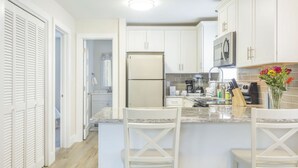 Une cuisine moderne avec des meubles blancs, un îlot central doté de tabourets, un réfrigérateur et un four à micro-ondes.