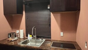 A kitchen with dark wooden cabinets, a stainless steel sink, and a countertop with various items. - Cozy 1-bedroom apartment in terrific Nassau with AC (Nassau)
