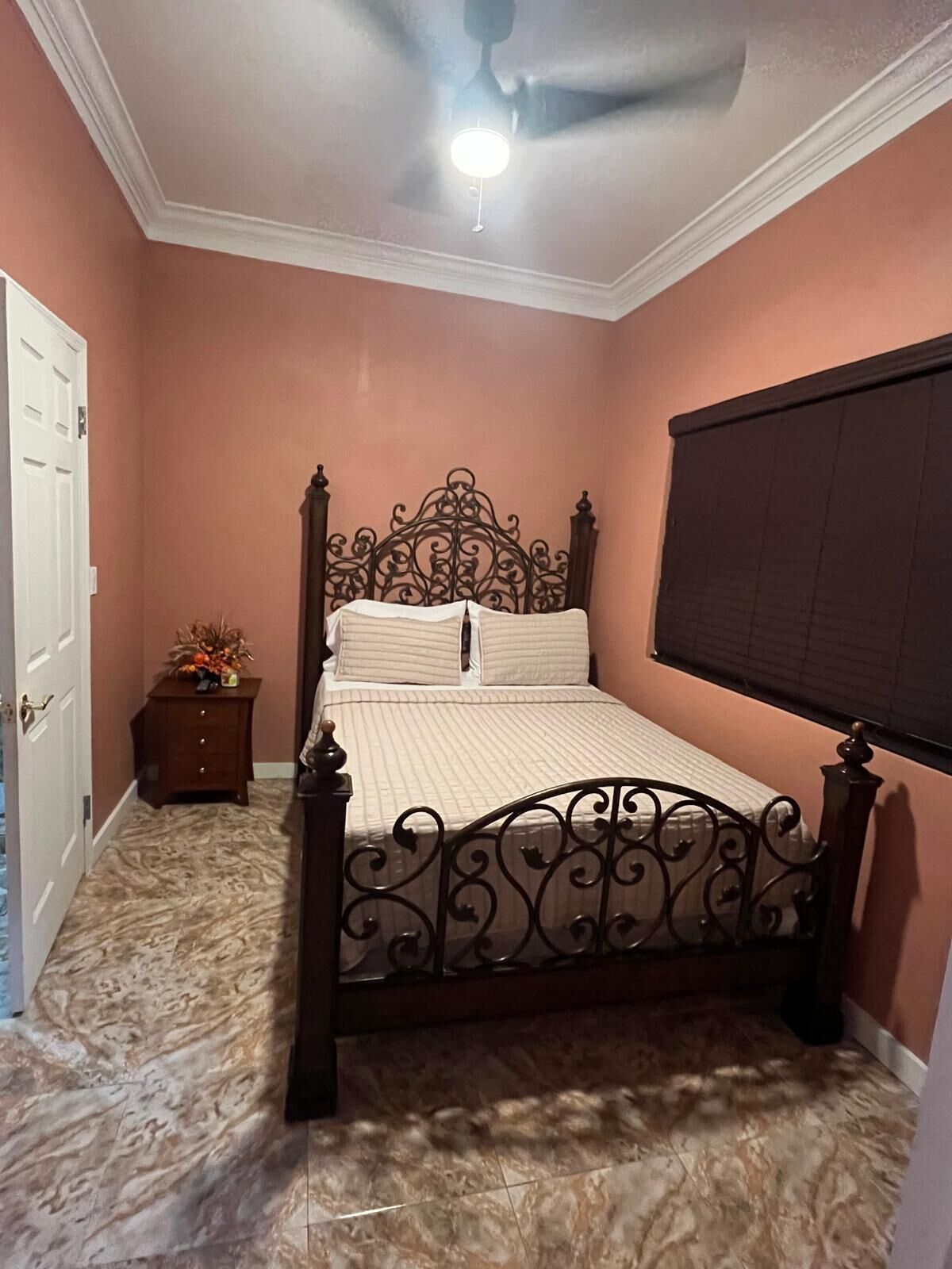 A bedroom with a bed, a ceiling fan, a nightstand, and a window with blinds.