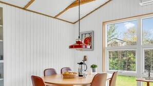 Ein Essbereich mit Holztisch, braunen Stühlen, einer roten Pendelleuchte und Blick auf Grünflächen.