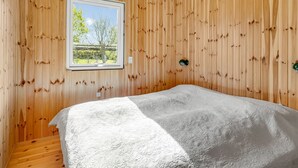 Ein Zimmer mit Holzwänden, einem Bett mit weißer Bettdecke, einem Fenster mit Blick auf Bäume und einer Hängelampe.