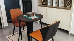 Ein stilvoller Essbereich mit einem runden Tisch, zwei Stühlen, einem kleinen Regal mit Dekoration und einer Tür im Hintergrund.