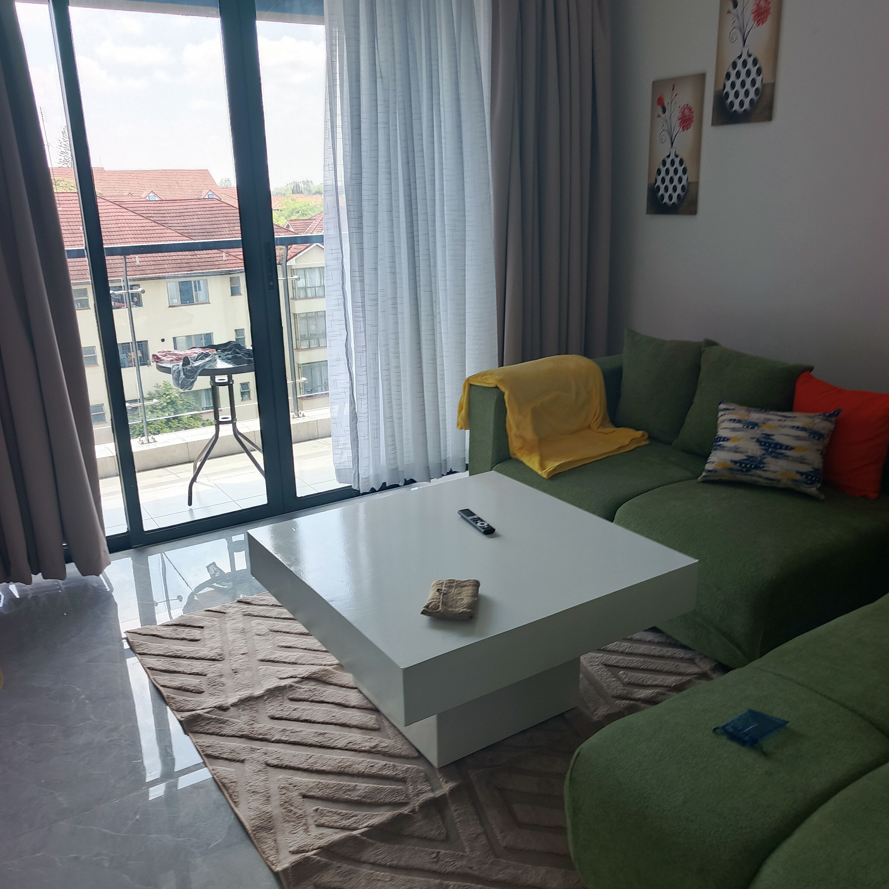 Un salon avec une table basse blanche, un canapé vert et une vue sur les immeubles par une grande fenêtre.