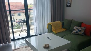 Ein Wohnzimmer mit einem weißen Couchtisch, einem grünen Sofa und Blick auf Gebäude durch ein großes Fenster.